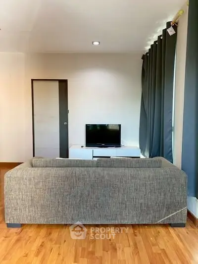 Modern living room with sleek sofa and TV, featuring elegant curtains and wooden flooring.