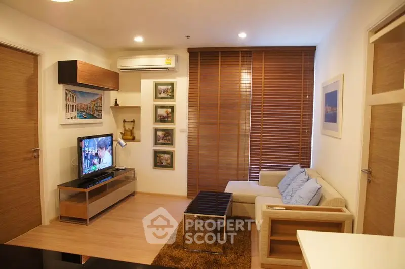 Cozy living room with modern decor, featuring a comfortable sofa, wall-mounted TV, and stylish wooden blinds.