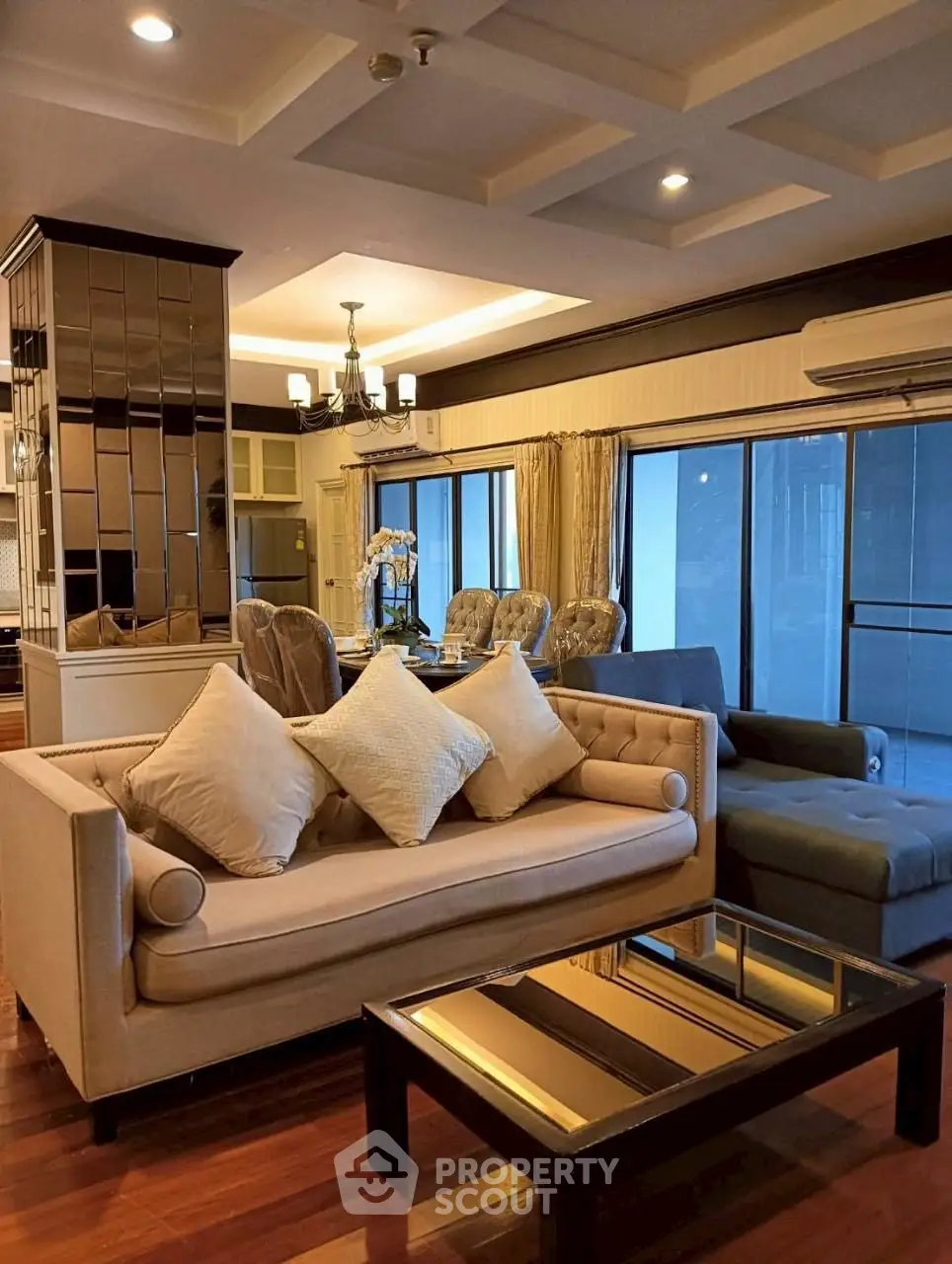 Luxurious living room with elegant sofa and dining area, featuring modern lighting and large windows.
