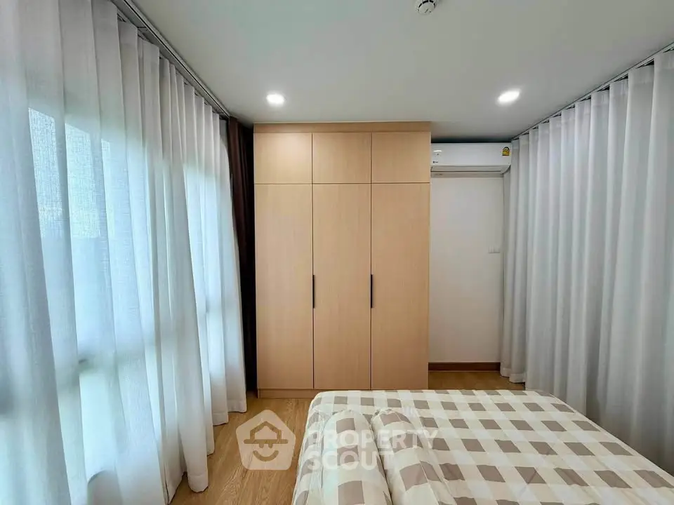 Cozy bedroom with wooden wardrobe and checkered bedding, featuring soft lighting and floor-to-ceiling curtains.