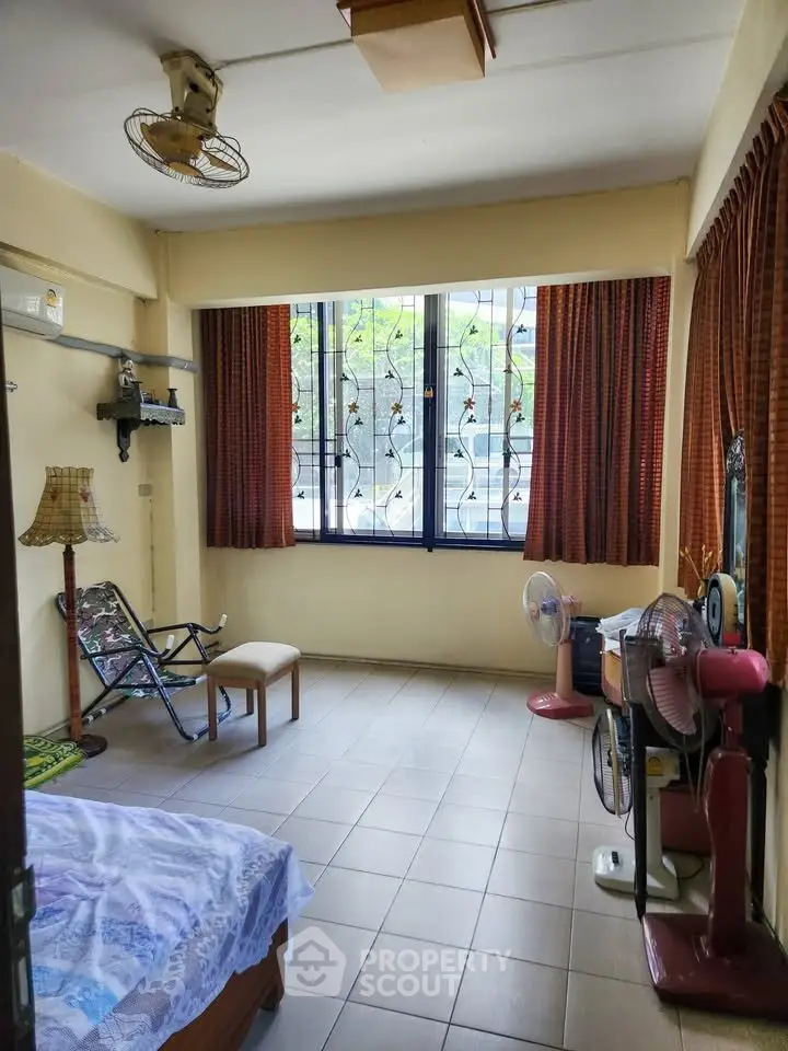 Cozy bedroom with large window and vintage decor, featuring a ceiling fan and comfortable seating area.
