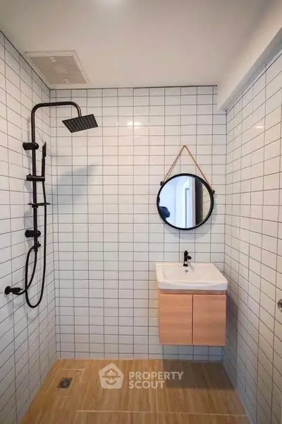 Modern minimalist bathroom with sleek black shower and round mirror.