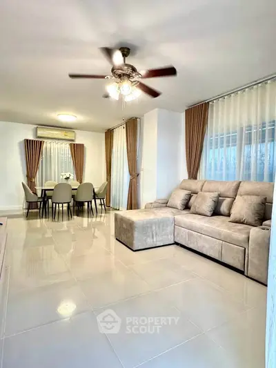 Spacious living room with modern decor and dining area, featuring elegant curtains and a ceiling fan.