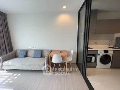 Modern living room with cozy sofa and dining area adjacent to sleek kitchen with washing machine.