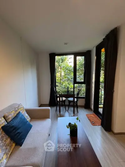 Cozy living room with large windows and garden view, featuring modern furniture and natural light.