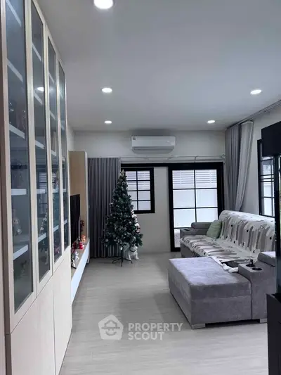 Modern living room with Christmas tree and stylish furniture, featuring a cozy sectional sofa and sleek cabinetry.