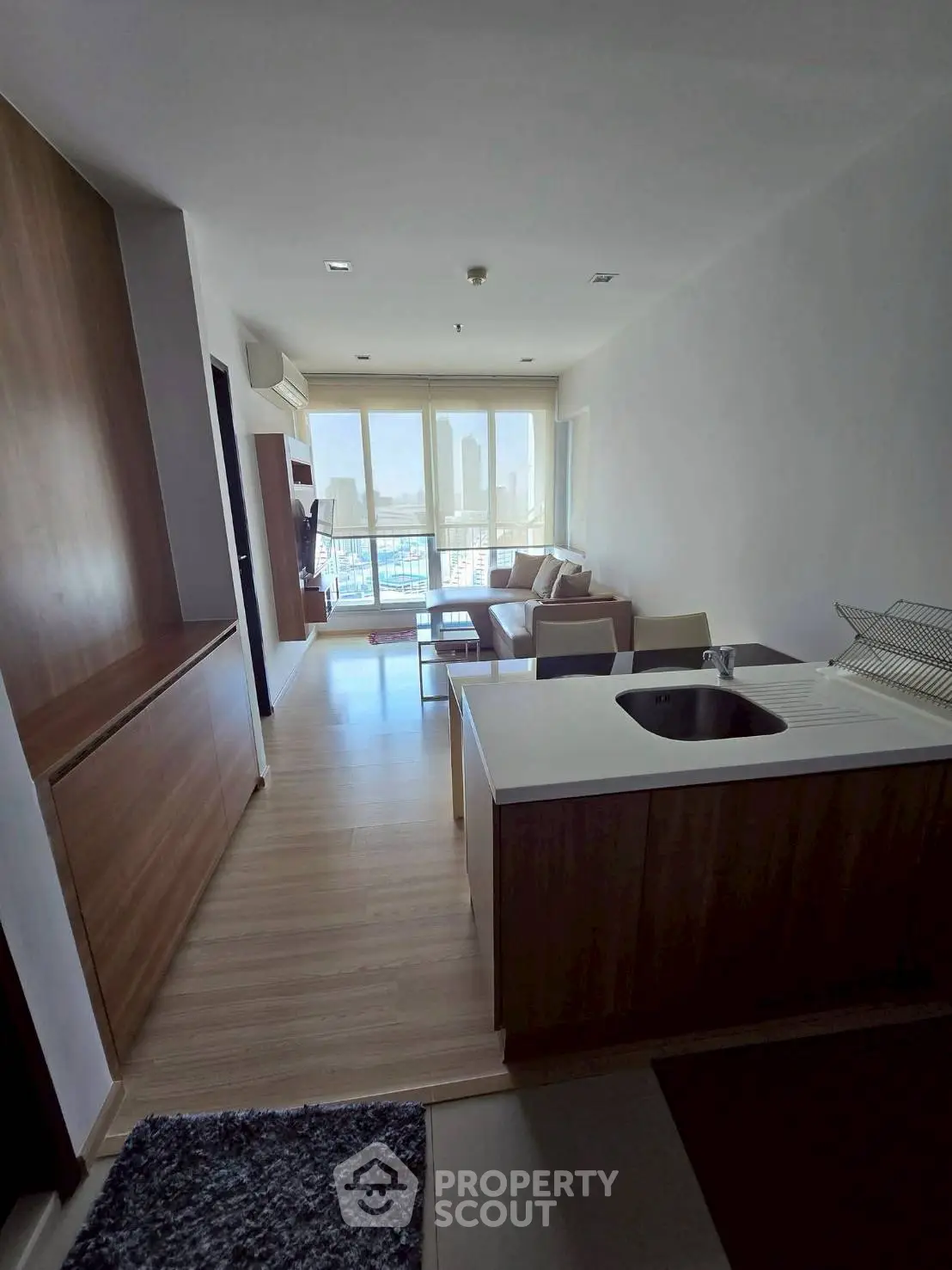 Modern open-layout living room with kitchen, featuring large windows and city view.