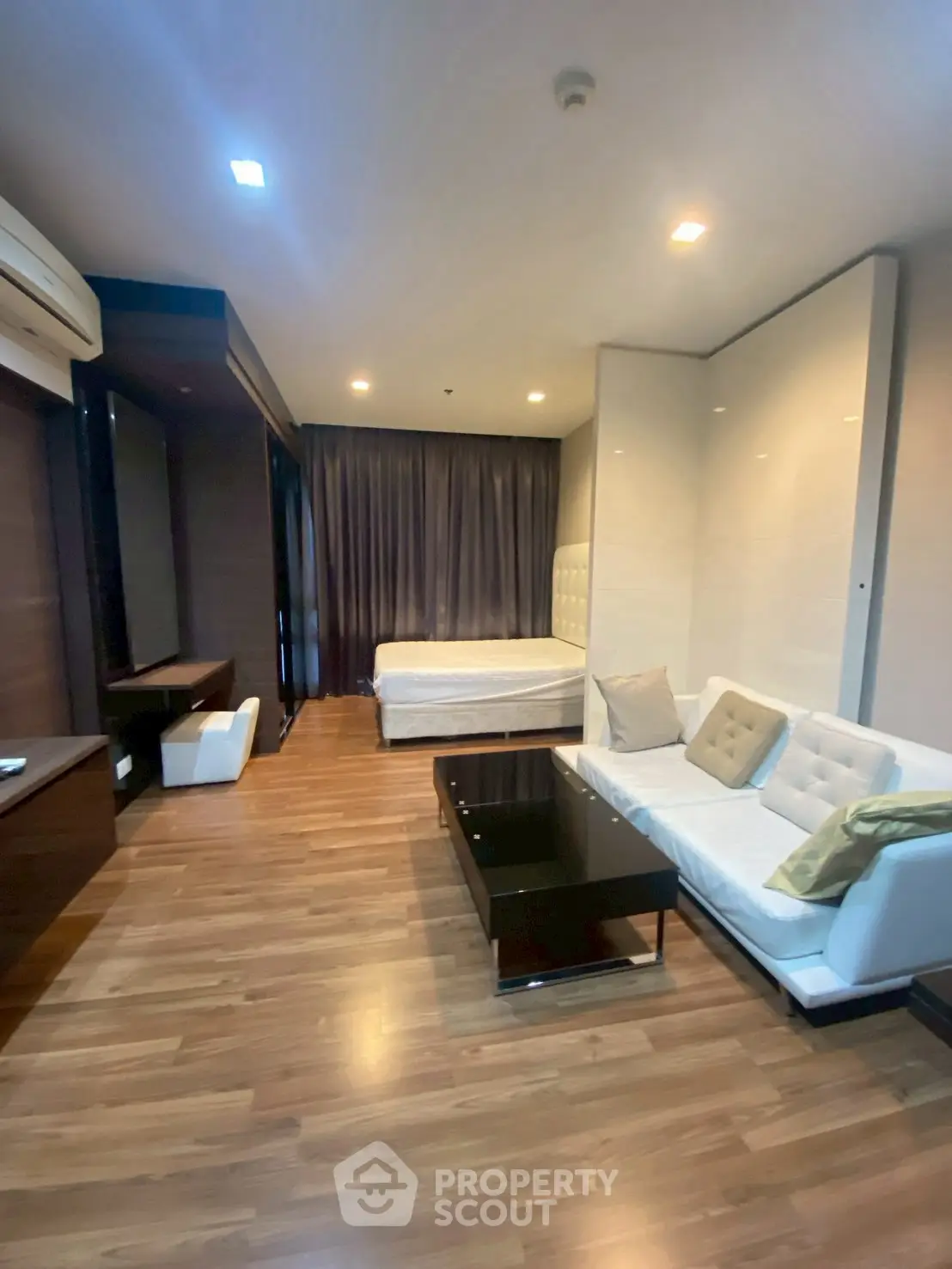 Modern studio apartment with stylish living area and cozy bed, featuring elegant wooden flooring.