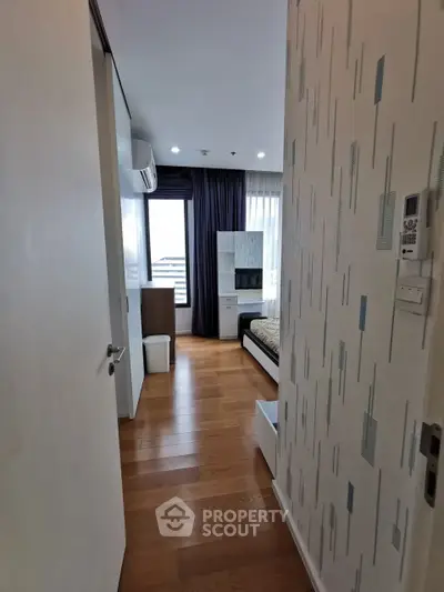 Modern bedroom with wooden flooring and stylish decor, featuring a large window for natural light.