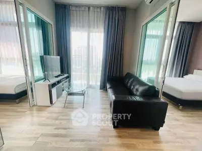 Modern living room with sleek black sofa and glass coffee table, featuring large windows and natural light.