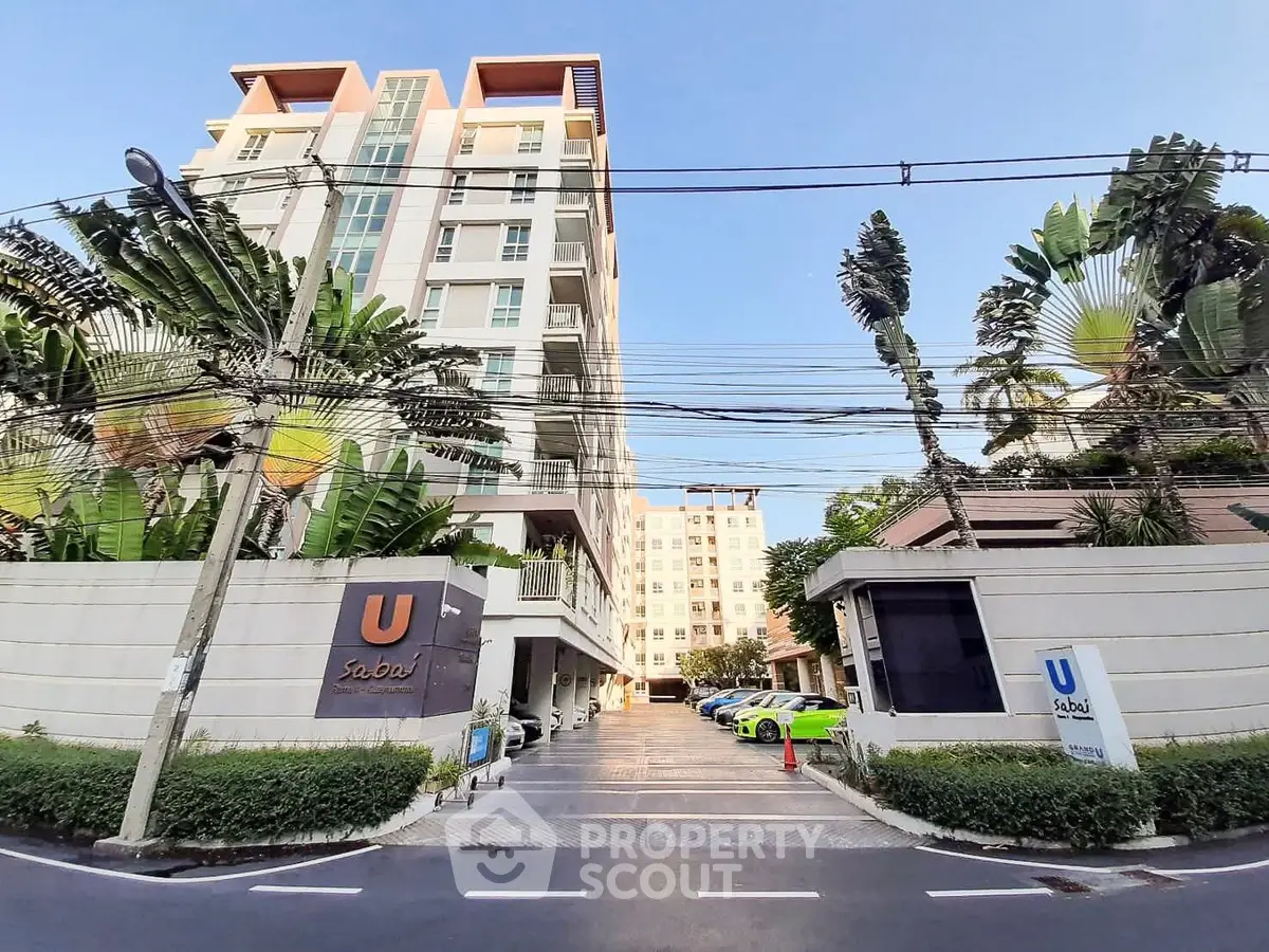 Modern condominium building with lush greenery and ample parking space.