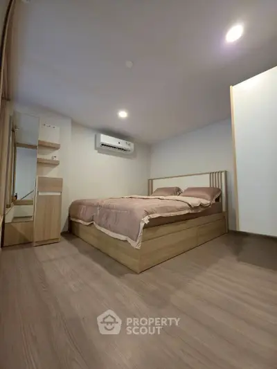 Modern bedroom with wooden flooring and stylish bed frame, featuring built-in storage and air conditioning.