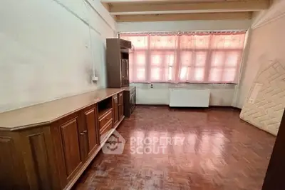 Spacious room with parquet flooring and large windows, featuring wooden cabinetry and natural light.