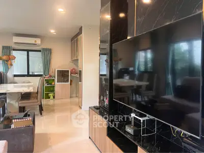 Modern living room with sleek TV setup and dining area, featuring stylish decor and ample natural light.