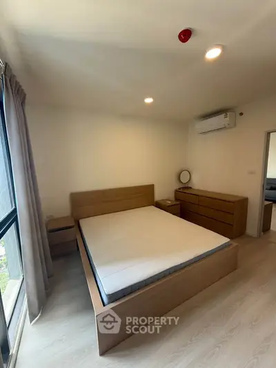 Modern bedroom with minimalist design featuring a wooden bed frame, dresser, and large window for natural light.