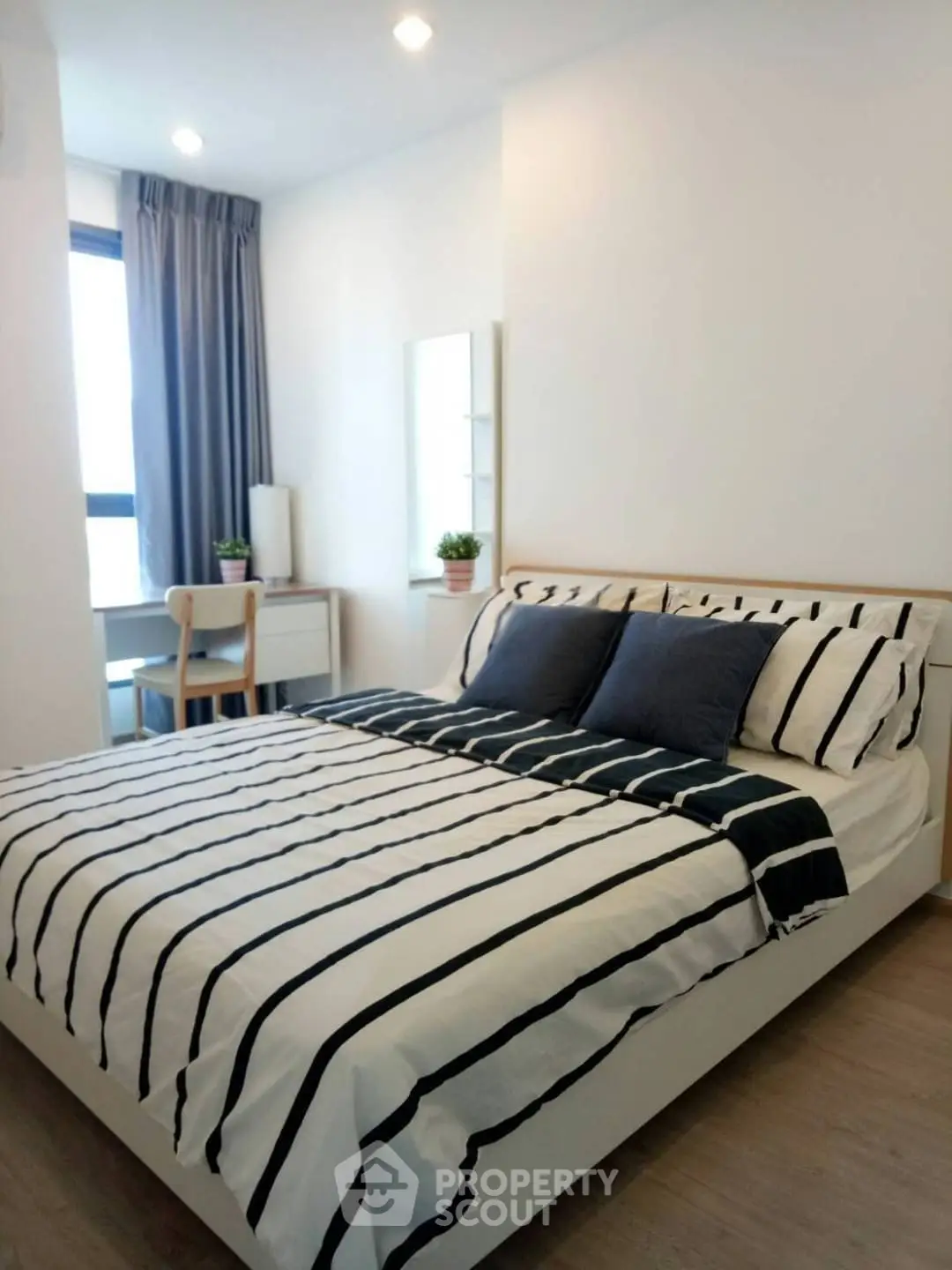 Modern bedroom with striped bedding and natural light, featuring a cozy workspace by the window.