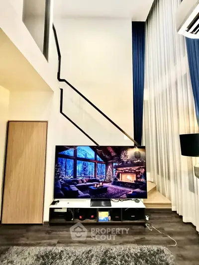 Modern living room with high ceilings and stylish decor, featuring a large TV and elegant staircase.