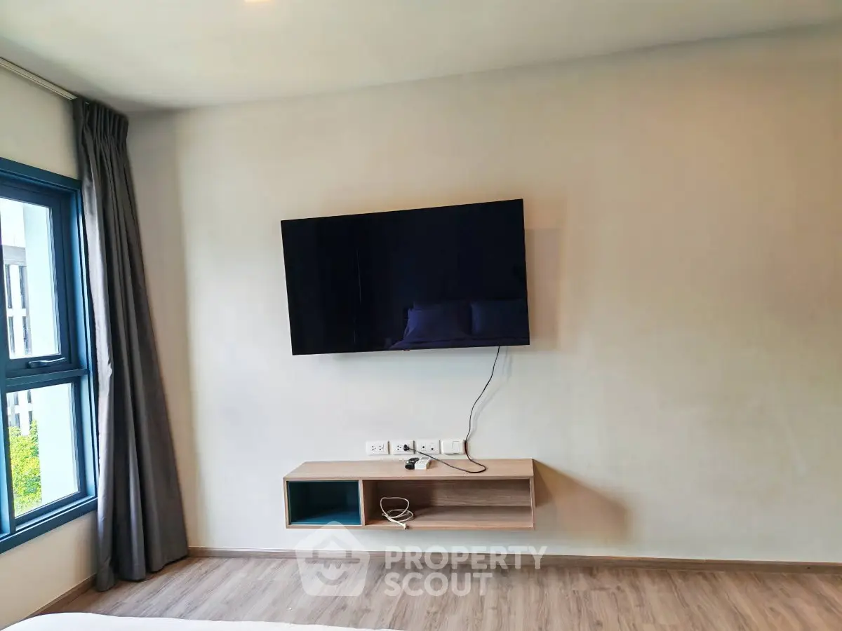 Modern living room with wall-mounted TV and sleek wooden shelf, featuring large window and stylish curtains.