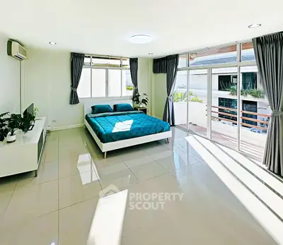 Spacious bedroom with large windows and balcony access, featuring modern decor and abundant natural light.