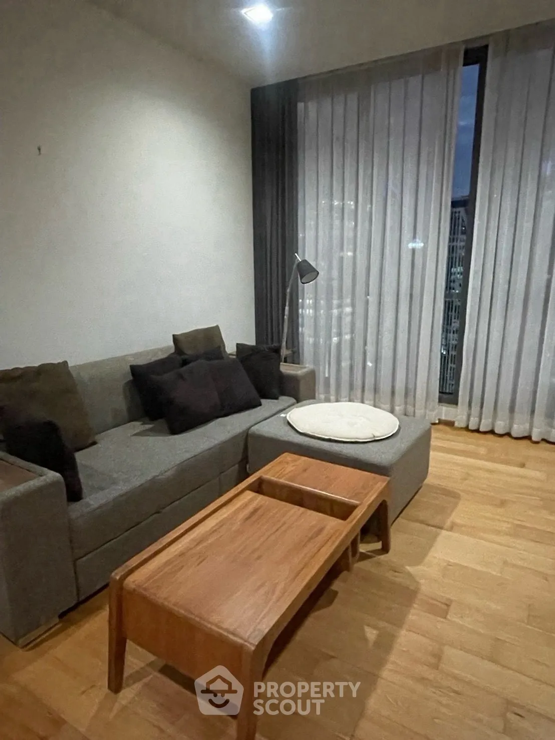 Modern living room with cozy gray sofa and wooden coffee table, featuring floor-to-ceiling windows.