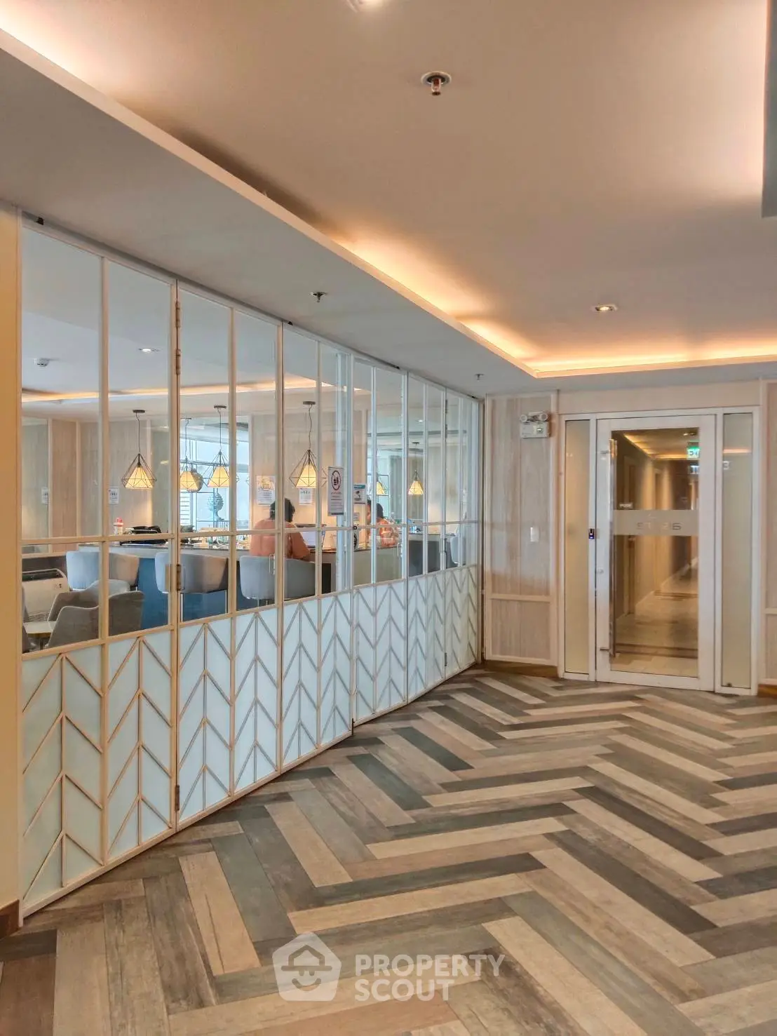 Modern lobby with stylish herringbone flooring and glass partitions in upscale building.