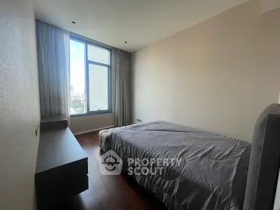 Cozy bedroom with large window and modern furnishings in a high-rise apartment.
