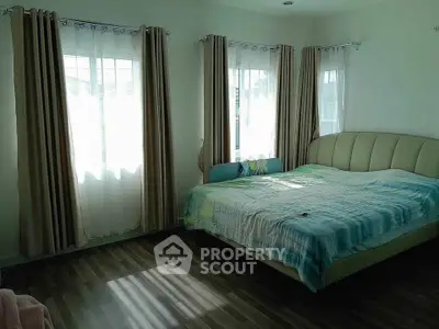 Bright bedroom with large windows and elegant curtains, featuring a stylish bed and wooden flooring.