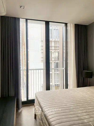 Modern bedroom with large windows and city view, featuring elegant curtains and a comfortable bed.