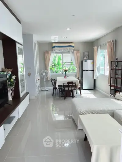 Spacious living room with modern decor and natural light, featuring a dining area and sleek appliances.