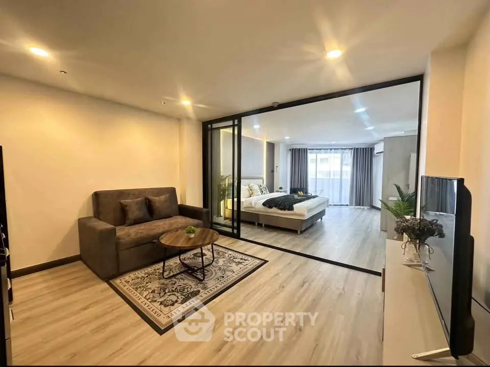 Spacious modern living room with glass partition leading to a cozy bedroom, featuring elegant decor and natural light.