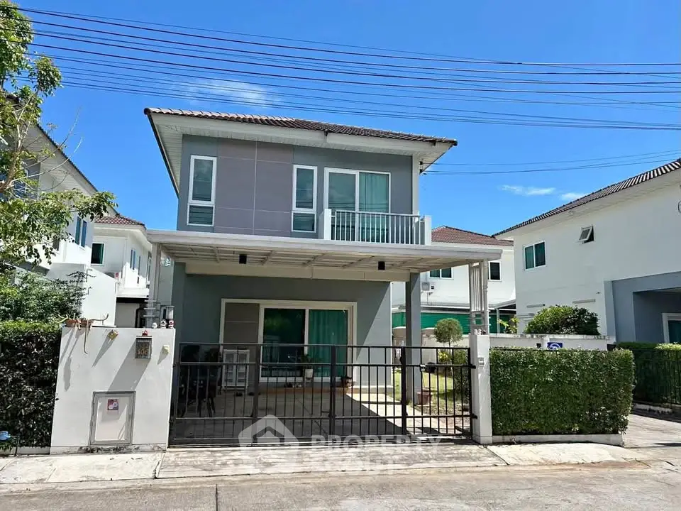 Modern two-story house with balcony and gated driveway in suburban neighborhood.