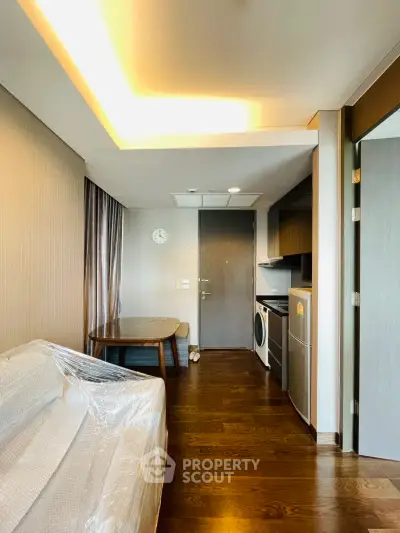 Modern apartment interior with sleek kitchen and cozy living area, featuring wooden flooring and stylish lighting.