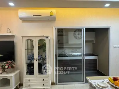 Cozy and well-lit living space featuring a classic white display cabinet, modern air conditioning unit, and sliding doors leading to a sleek kitchen area.