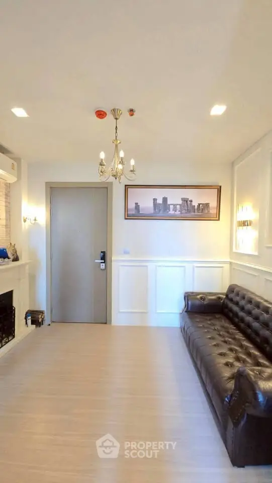 Elegant living room with leather sofa and chandelier, featuring modern decor and framed cityscape art.