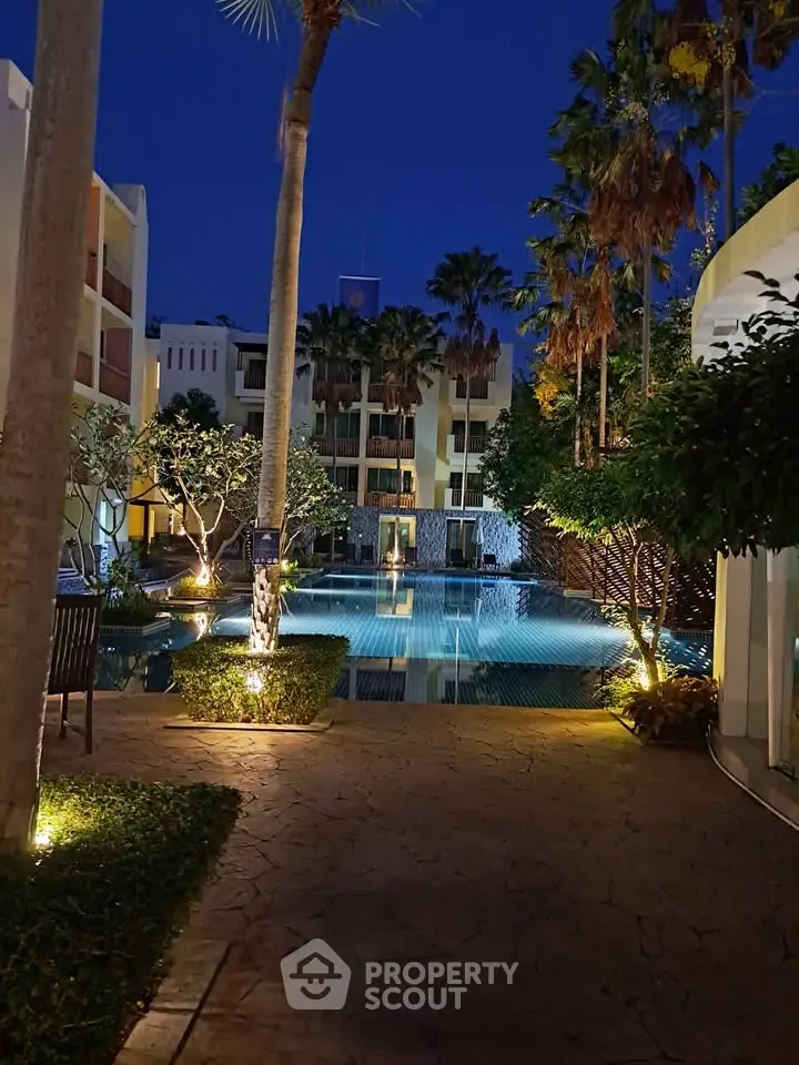 Luxurious poolside view at night with illuminated palm trees and modern architecture.