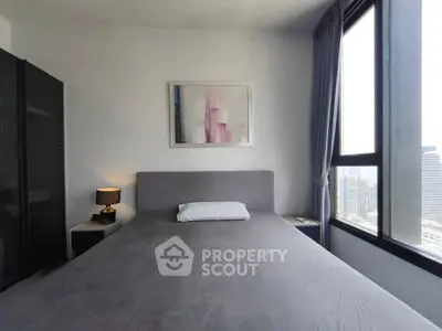 Modern bedroom with large windows offering city views, featuring a stylish bed and contemporary decor.