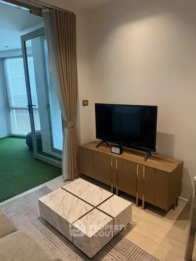 Modern living room with sleek TV stand and marble coffee table, opening to a balcony with green flooring.