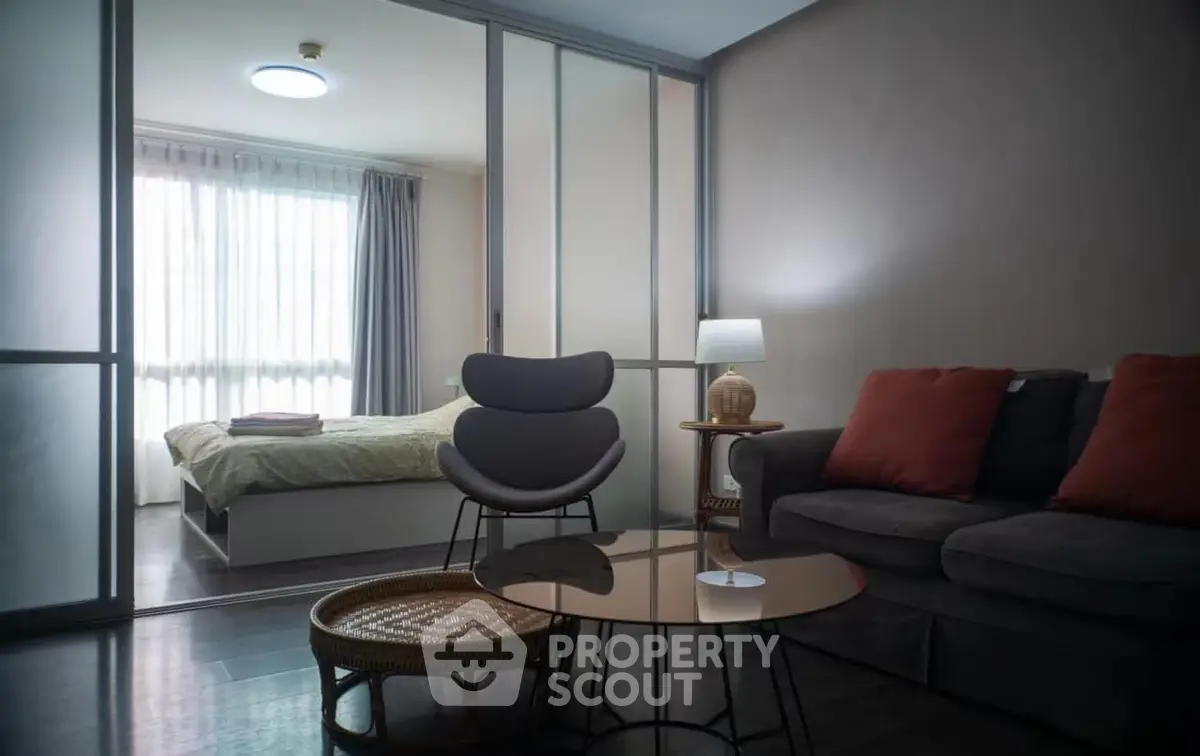 Modern living room with stylish furniture and a view into a cozy bedroom through sliding glass doors.