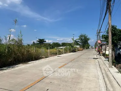 Scenic suburban road with lush greenery and clear blue sky, ideal for peaceful living.