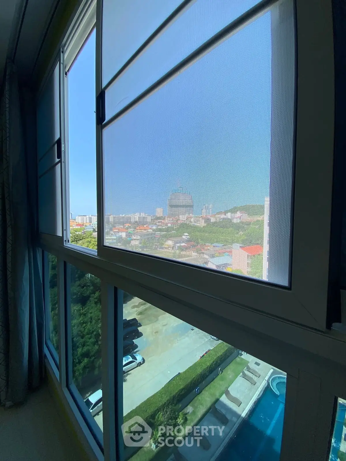 Stunning cityscape view from a modern apartment window overlooking a pool and lush greenery.