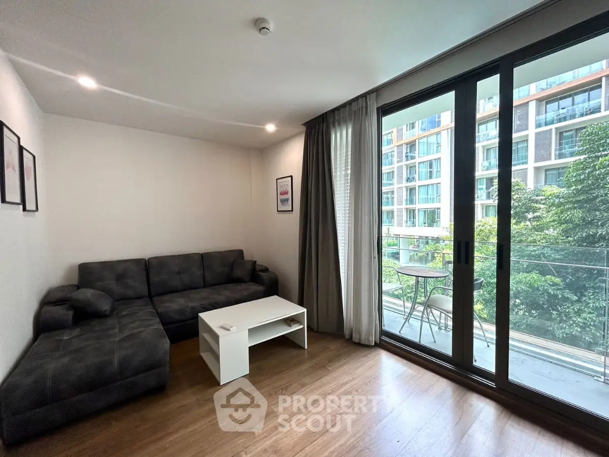 Modern living room with large glass doors opening to a balcony with a view of greenery.