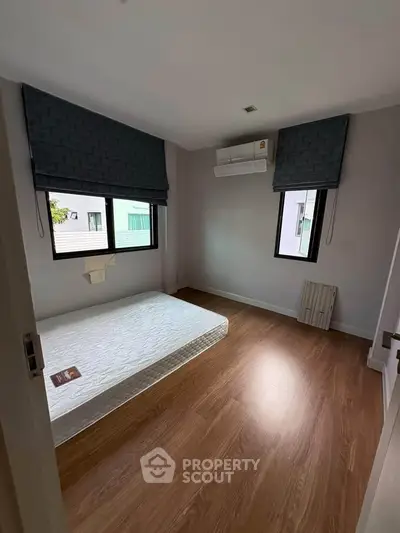 Spacious bedroom with wooden flooring and natural light, featuring a minimalist design and air conditioning.