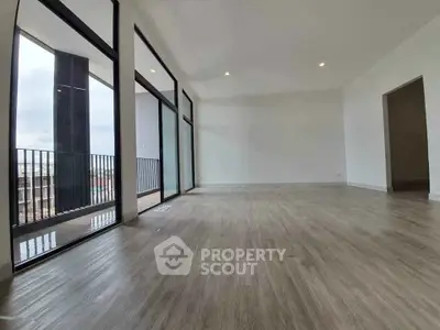Spacious modern living room with large windows and balcony access, featuring sleek flooring and ample natural light.