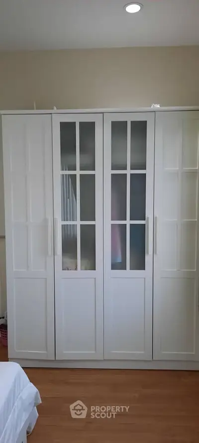 Spacious white wardrobe with glass panel doors in a cozy bedroom setting.