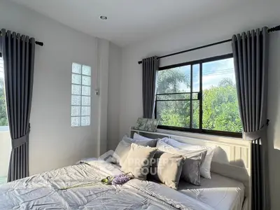 Bright and airy bedroom with large window and lush greenery view, perfect for relaxation.