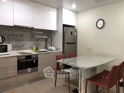 Modern kitchen with sleek cabinets, dining table, and stainless steel appliances.