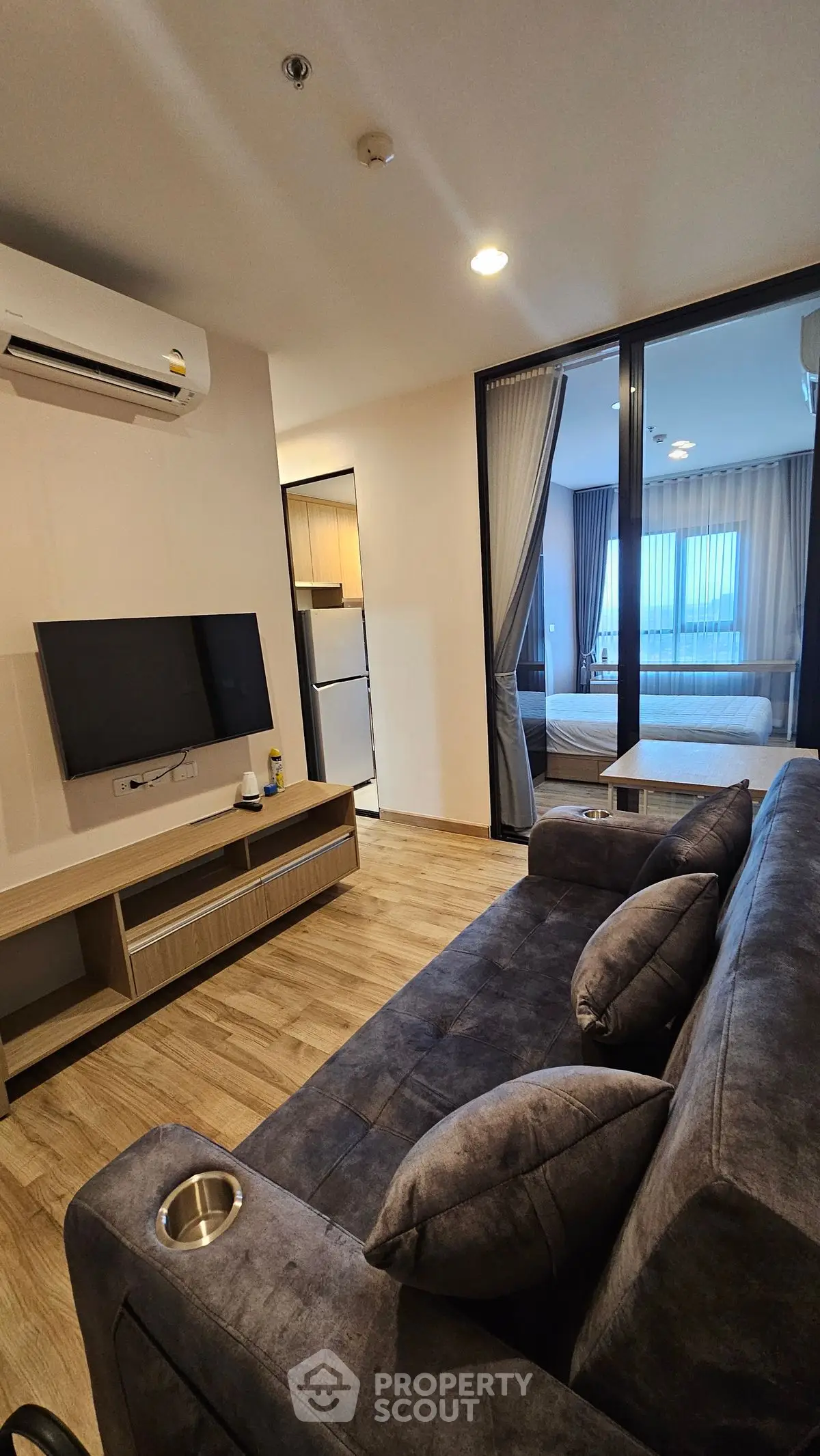 Modern living room with sleek sofa, wall-mounted TV, and view into cozy bedroom.