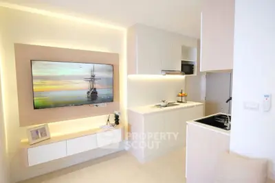 Modern living room with sleek kitchen, featuring built-in TV and minimalist design.