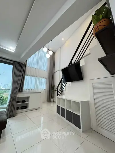 Modern living room with high ceiling and large windows offering city views.