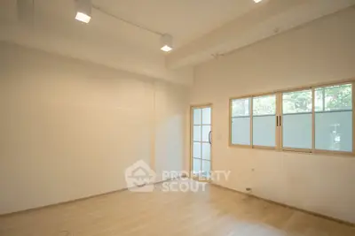 Spacious empty room with wooden flooring and large windows, perfect for customization.